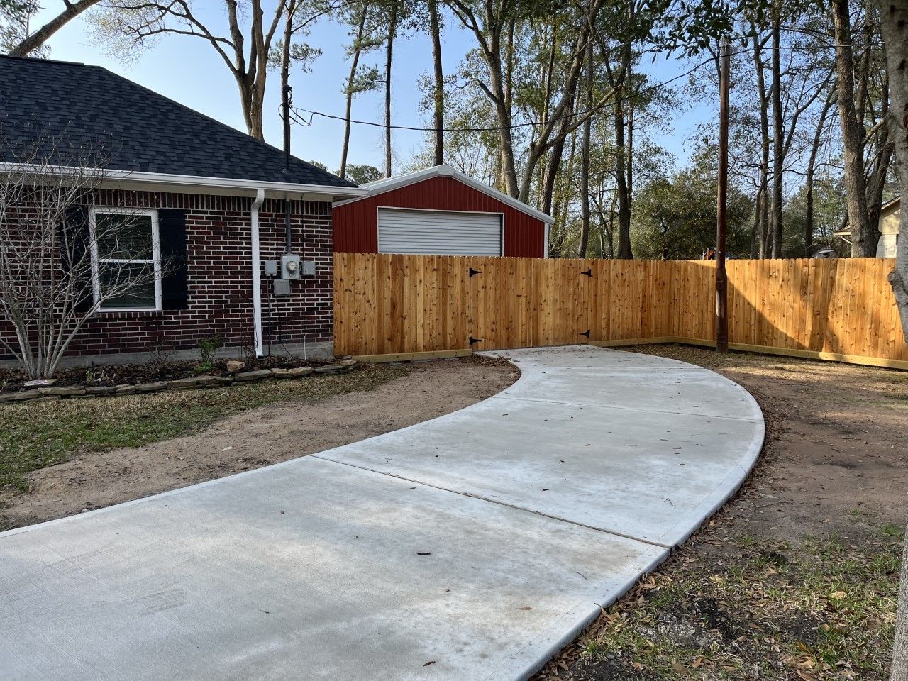 A brick house with a wooden fence and a concrete driveway leading to it.