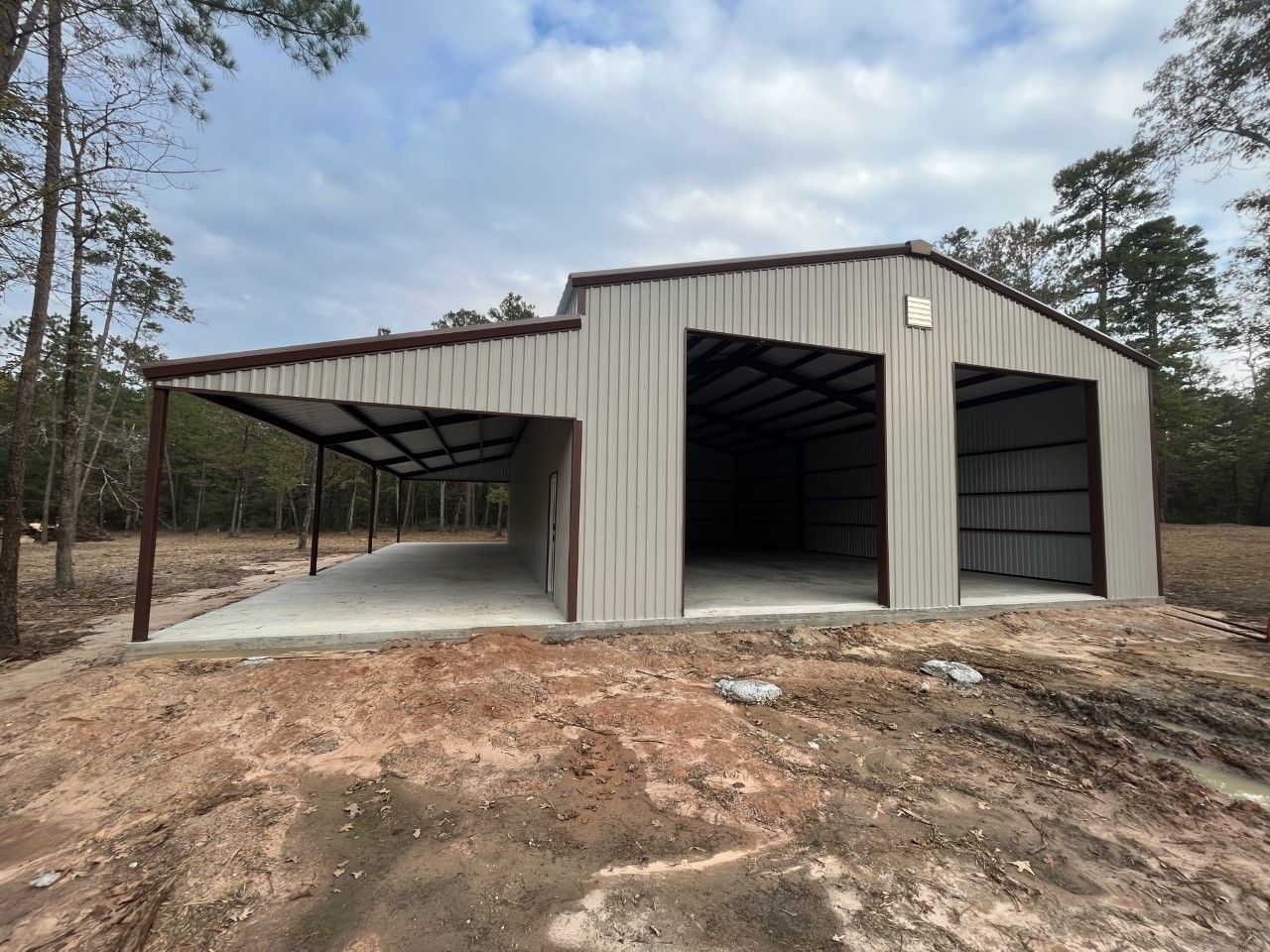 A metal building with two garage doors is sitting in the middle of a dirt field.