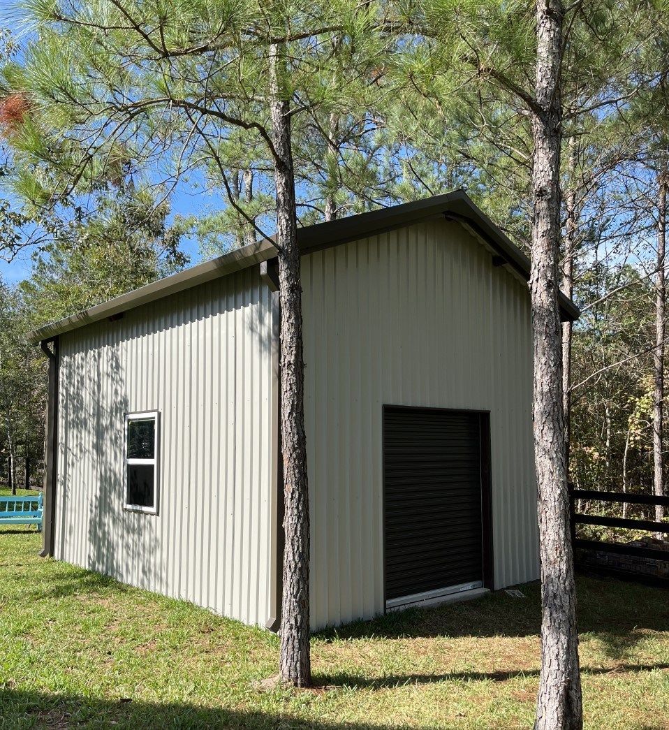A small white building with a garage door is surrounded by trees.