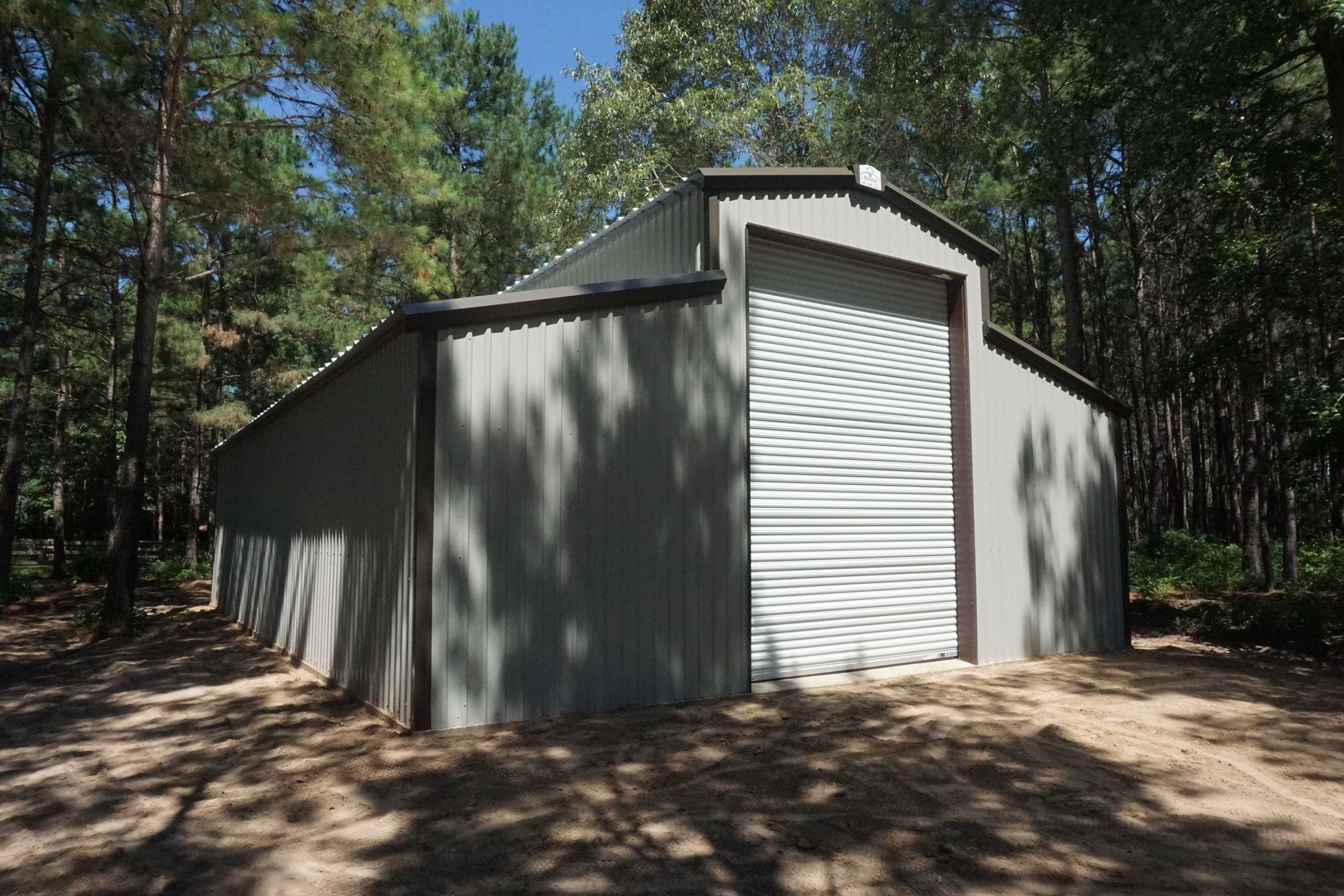 A large gray building with a white door is in the middle of a forest.
