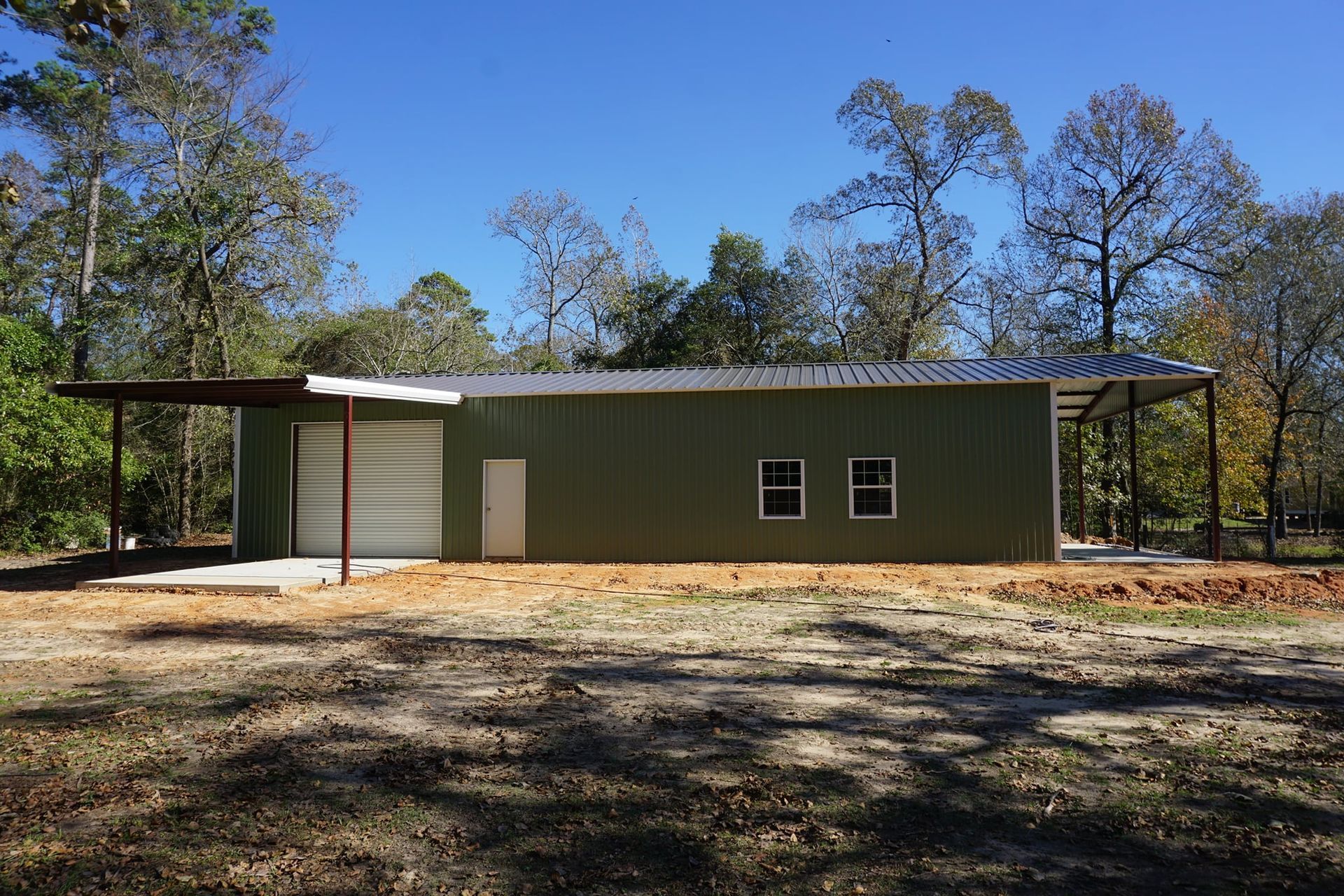A green metal building with a porch and trees in the background
