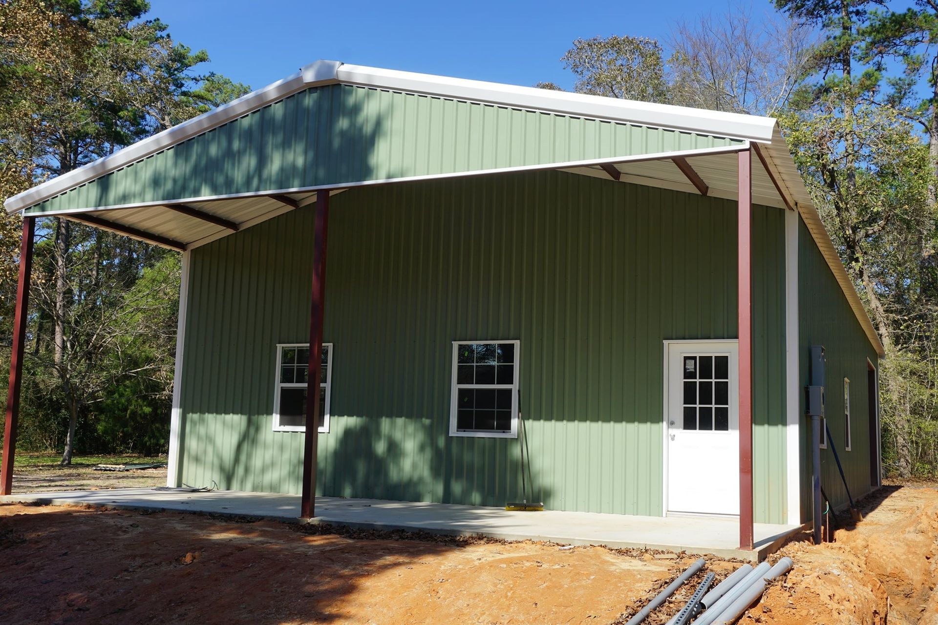 A green metal building with a porch and a white door.