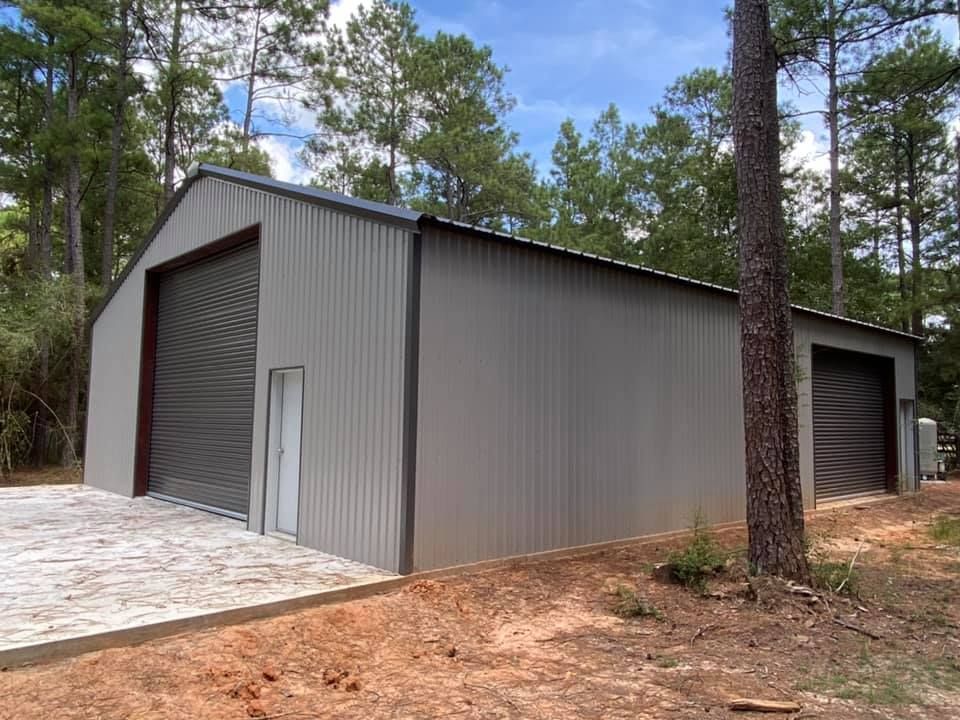 A large metal building with two garage doors is surrounded by trees.