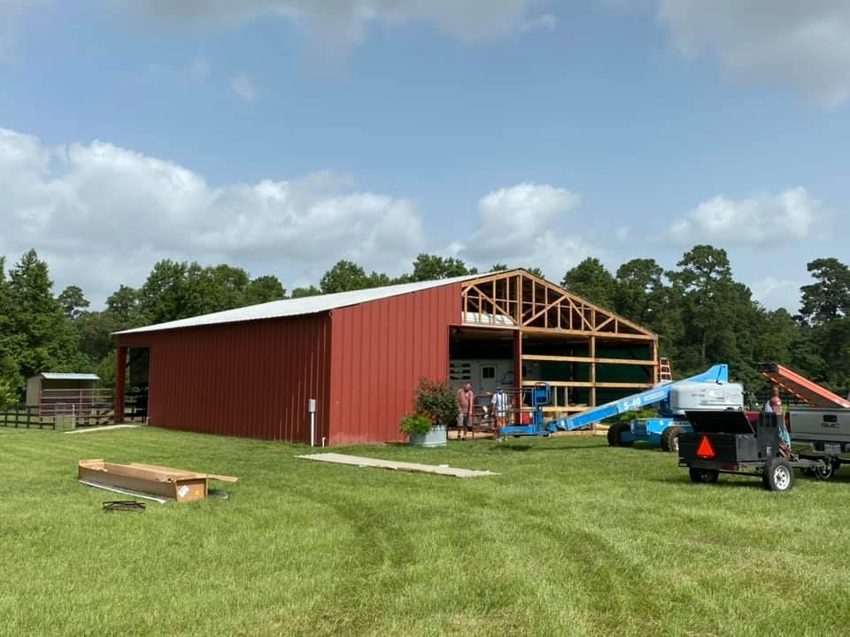A large red barn is being built in a grassy field.