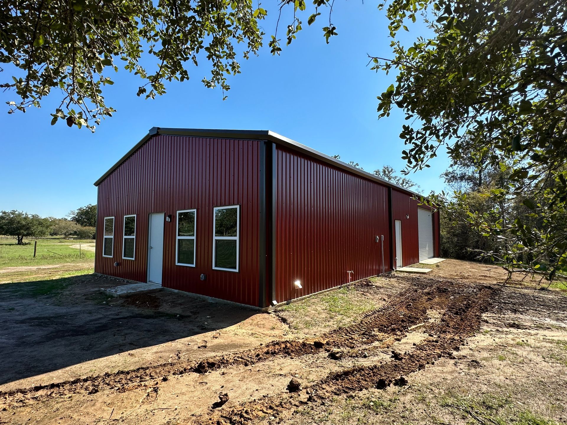 A red barn with a black roof is sitting in the middle of a dirt field.