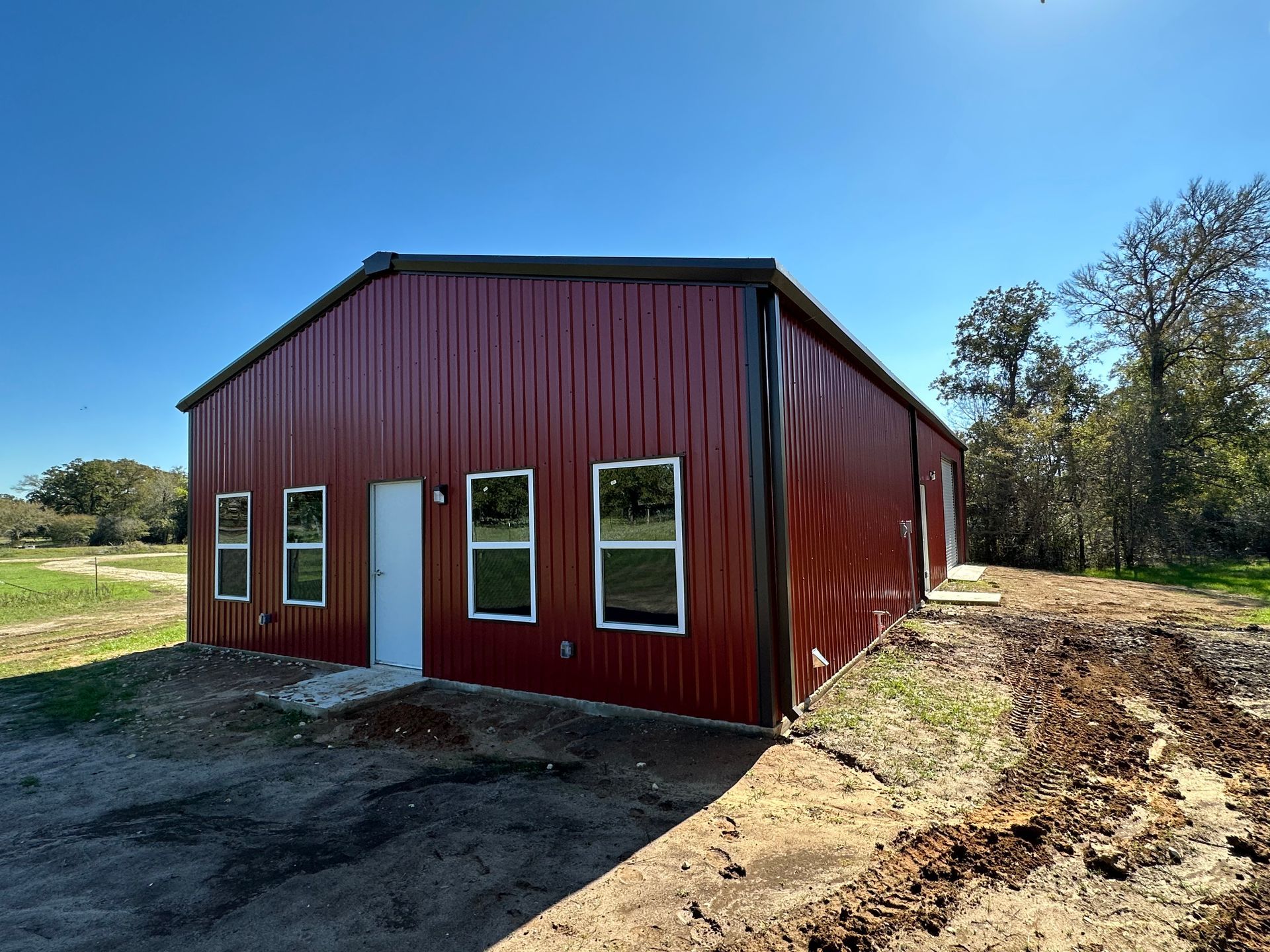 A red building with a lot of windows is sitting in the middle of a dirt field.