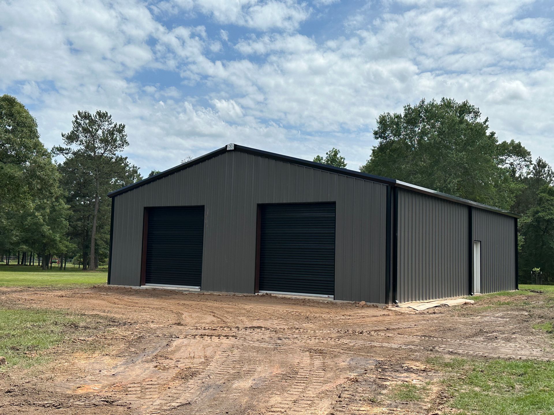 A large metal building with two garage doors is sitting in the middle of a dirt field.