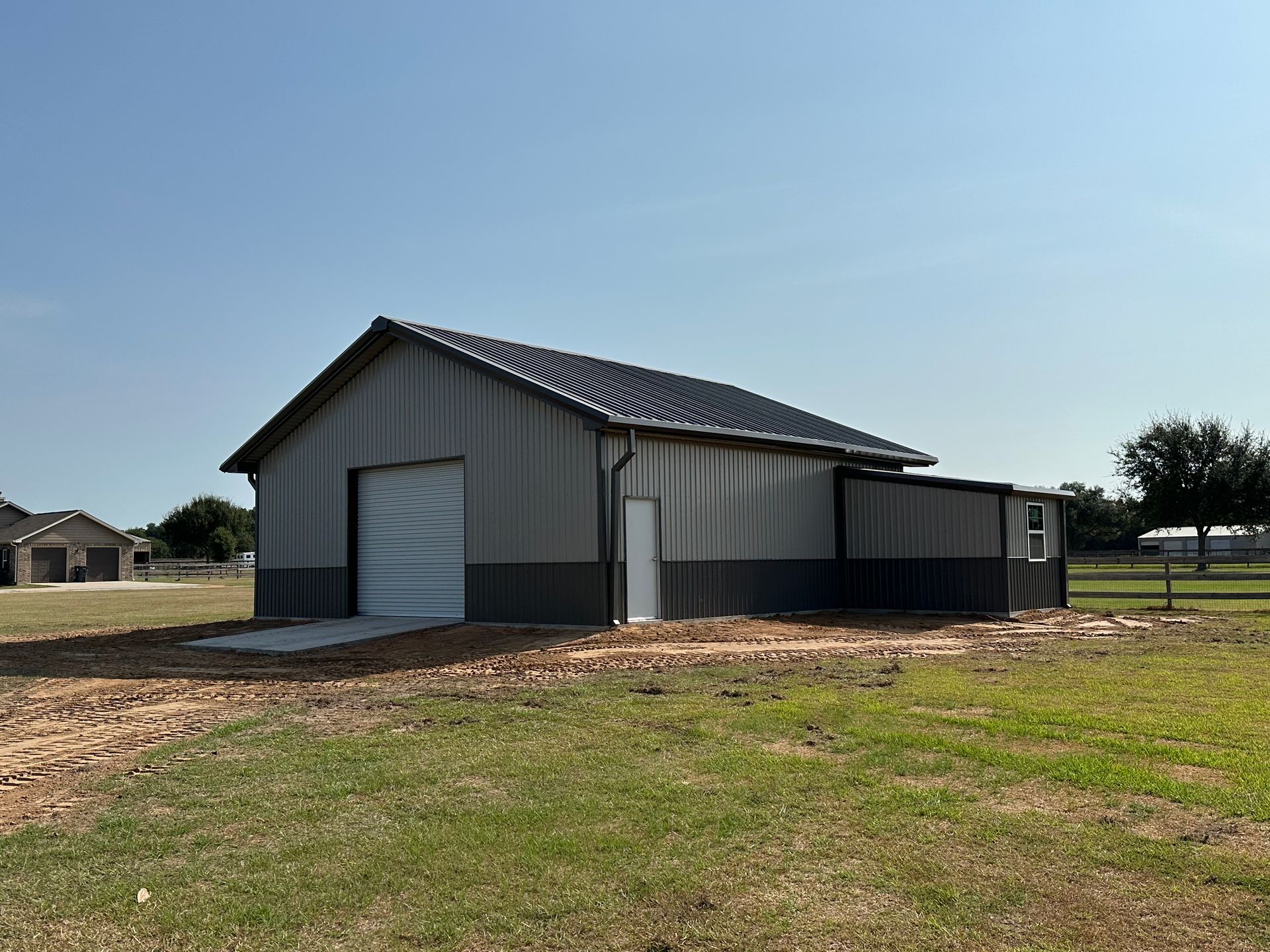 A large metal building with a garage door is sitting in the middle of a grassy field.