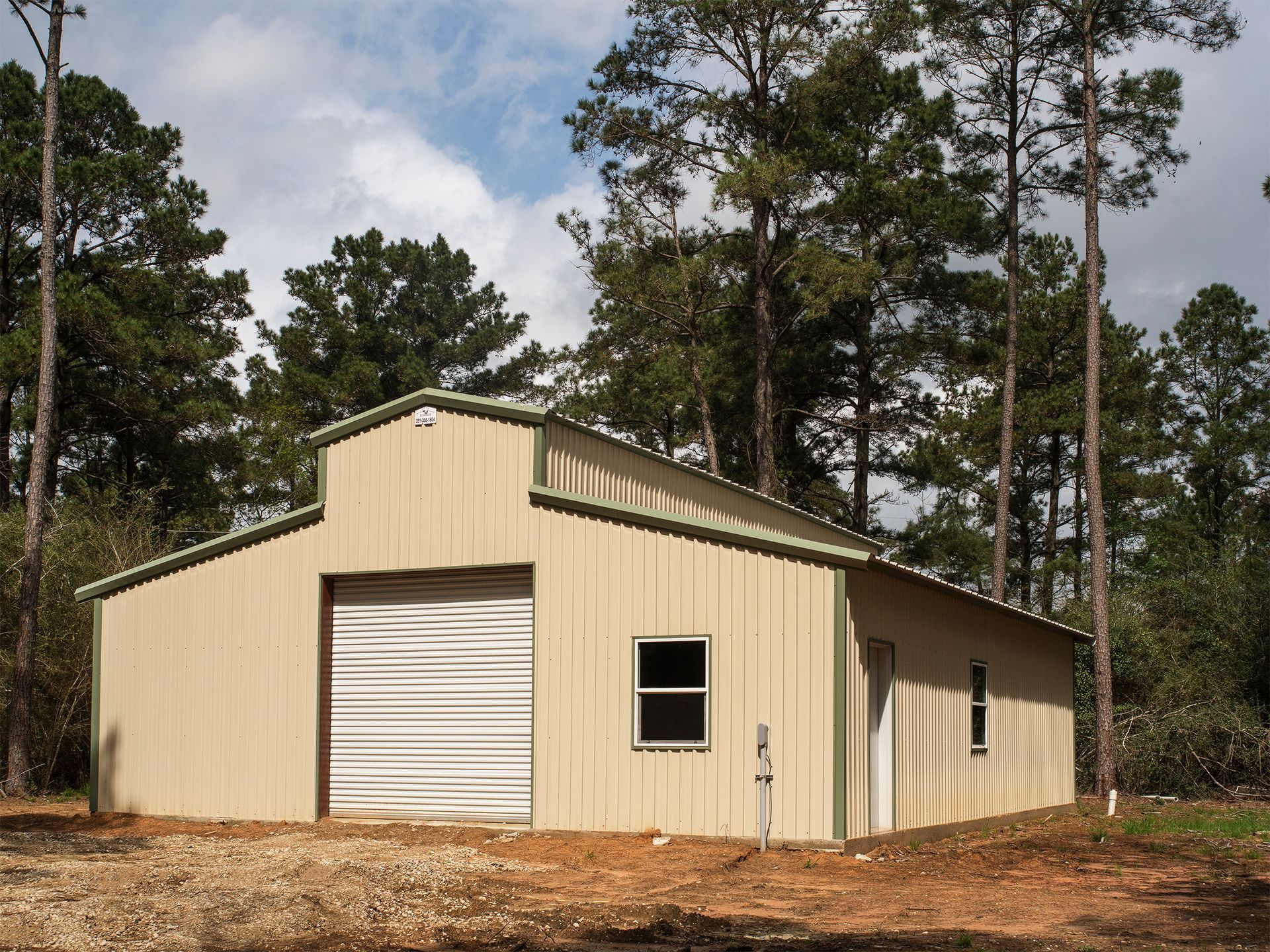 A tan building with a white garage door is surrounded by trees