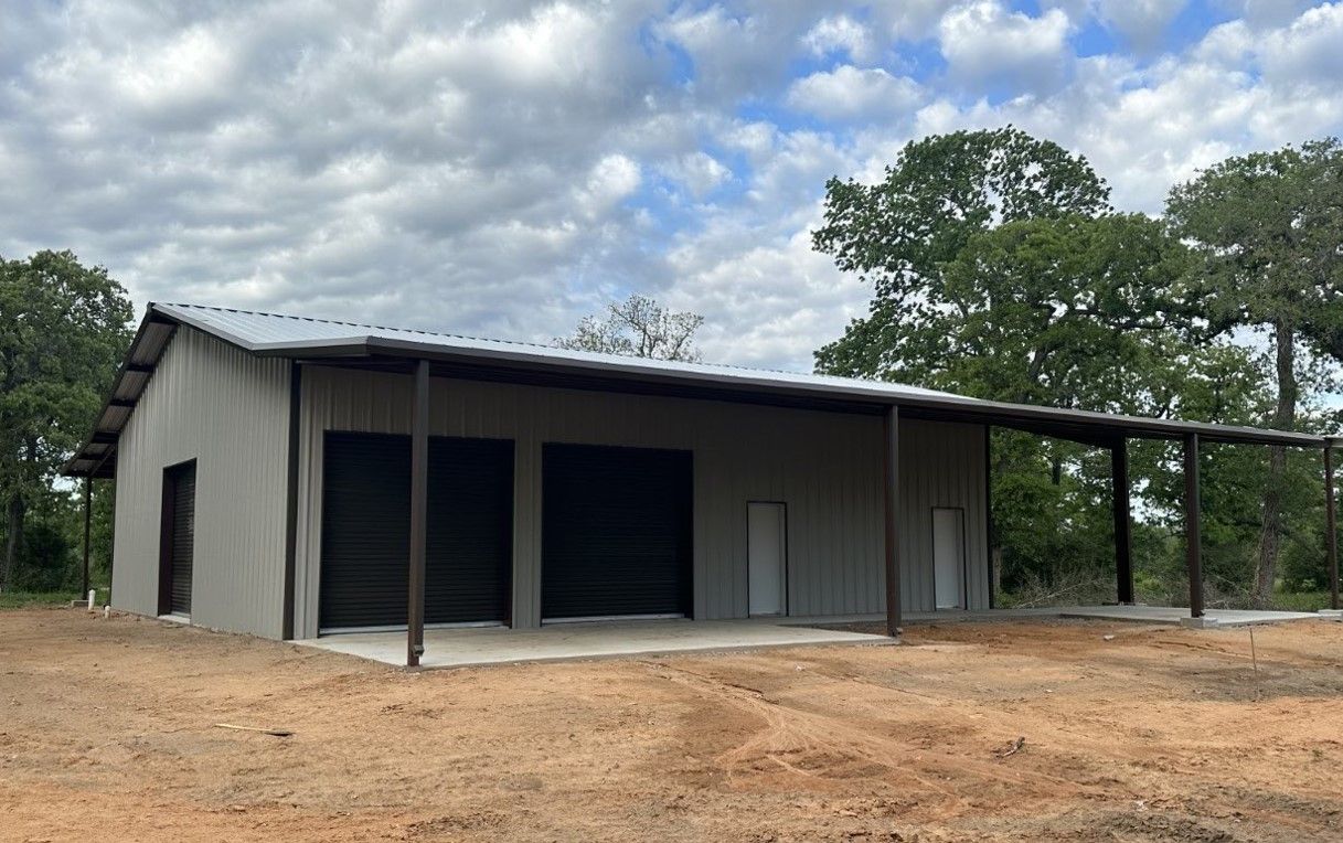 A large metal building with a covered porch is sitting in the middle of a dirt field.