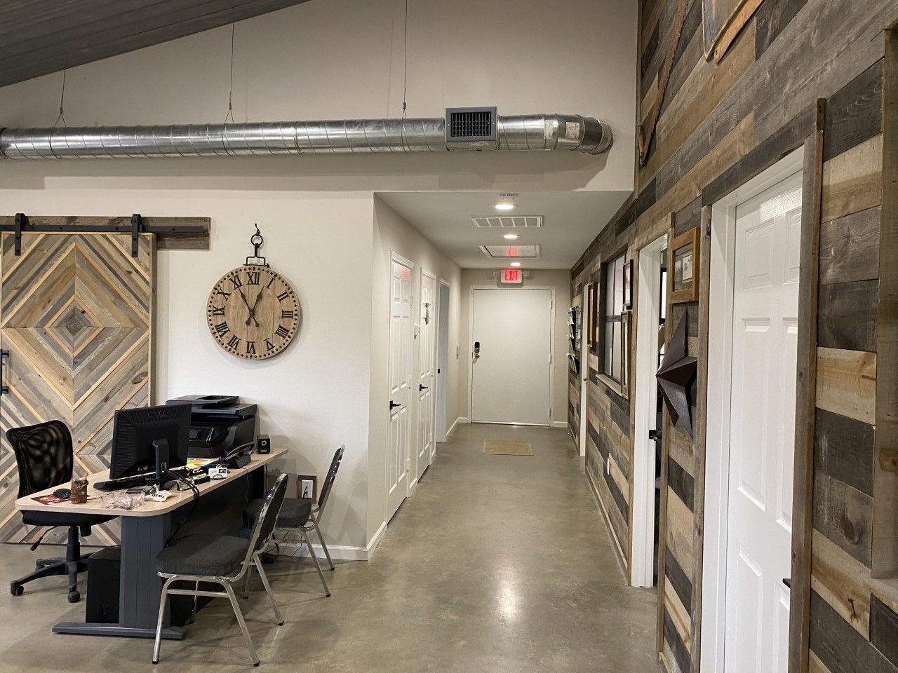 A long hallway with a clock on the wall and a desk and chairs.