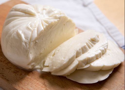 A piece of mozzarella cheese is sitting on a wooden cutting board.