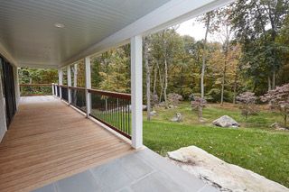 Covered wooden porch overlooking a green yard and wooded landscape