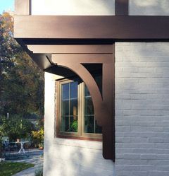 Exterior corner of a house with brown trim, arched support, and a window beside a white brick wall.