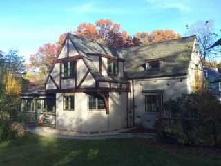 Tudor-style house with cream walls and dark timber trim, set among autumn trees in daylight.