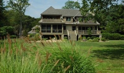A large multi-story home with a screened-in porch and balcony, set behind tall green grasses and a grassy lawn.