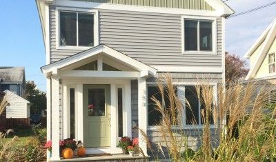 A two-story grey house with white trim, a covered front porch, a light green door, and fall pumpkins at the entrance.