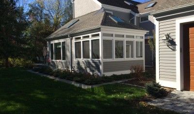 A grey-sided home extension with large windows and a skylight roof, surrounded by a lawn and landscaped garden.