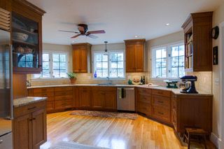 Bright wooden kitchen with cabinets, large windows, and a ceiling fan on hardwood floors