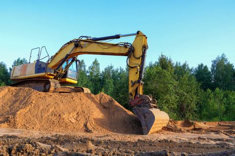 A yellow excavator is sitting on top of a pile of dirt.