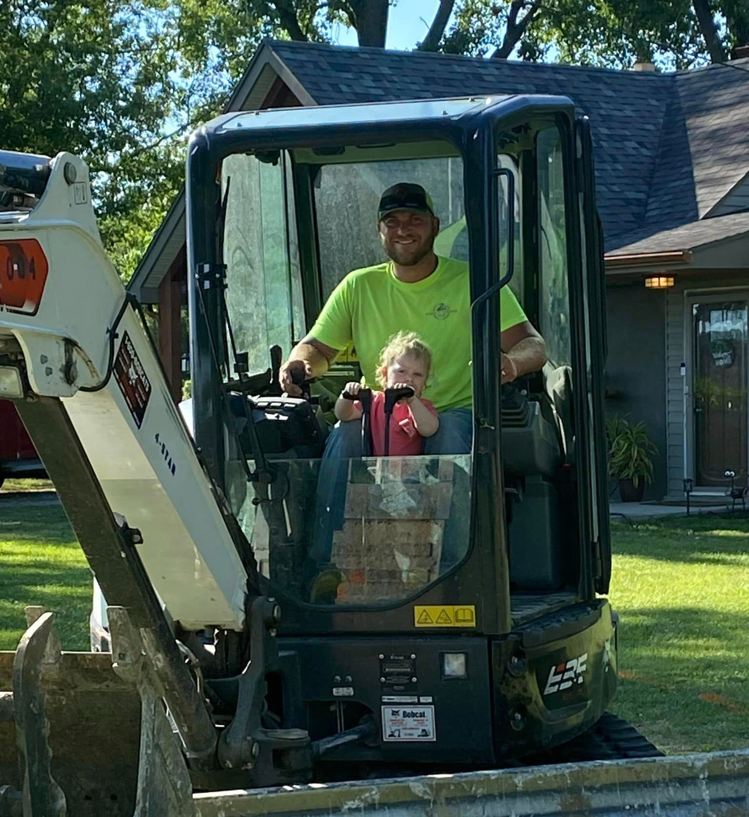A man and child are sitting in a bobcat excavator