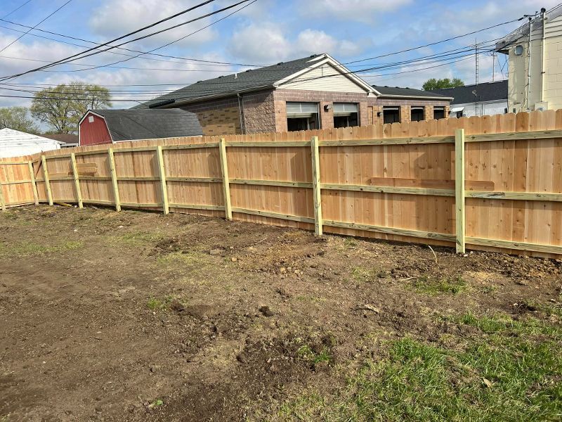 A wooden fence is sitting in the middle of a dirt field in front of a house.