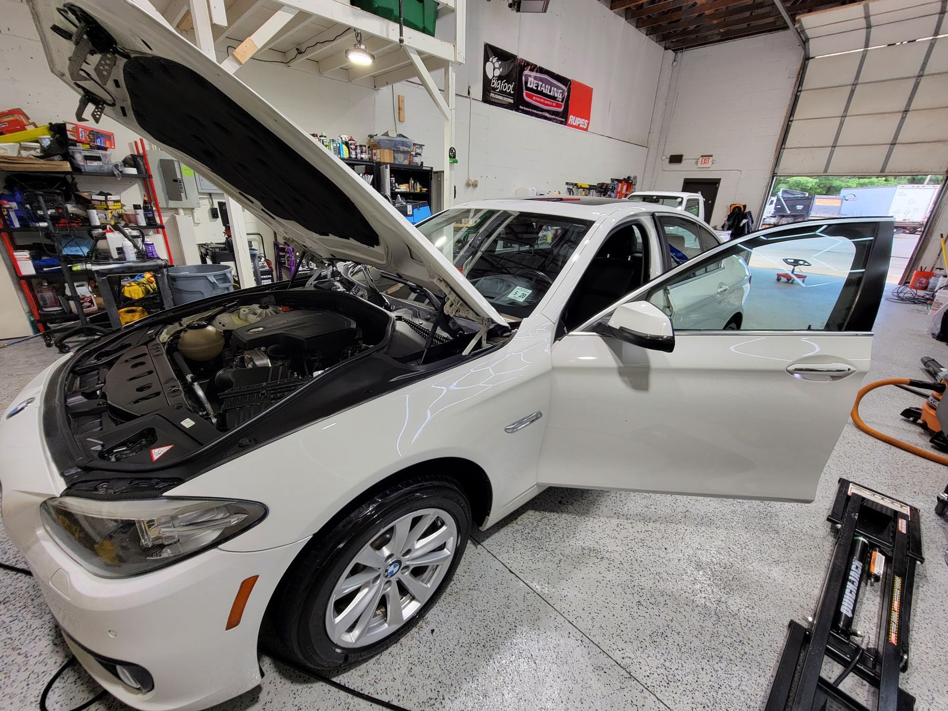 A white car is being worked on in a garage with the hood up.