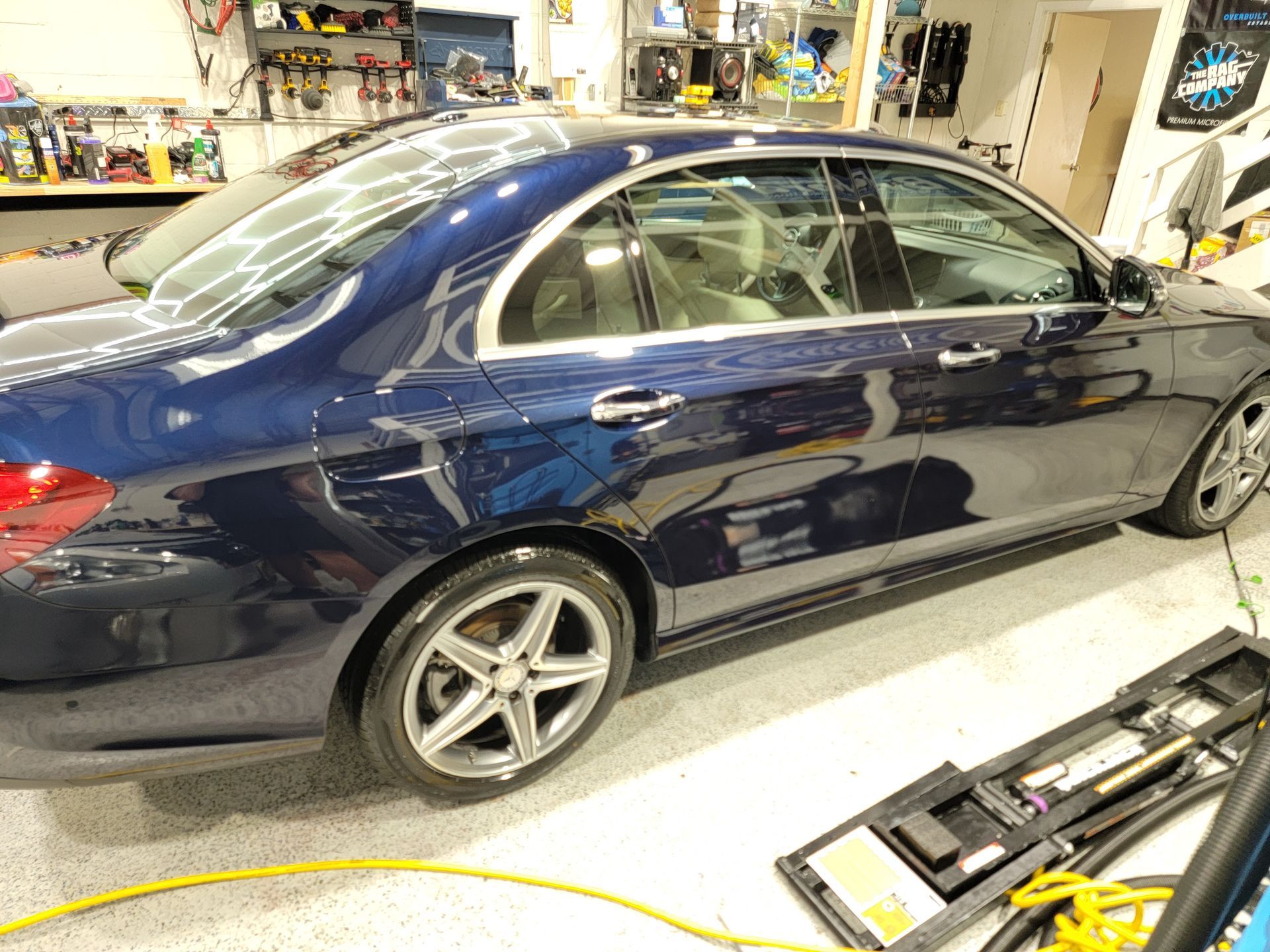 A blue car is parked in a garage next to a yellow hose.