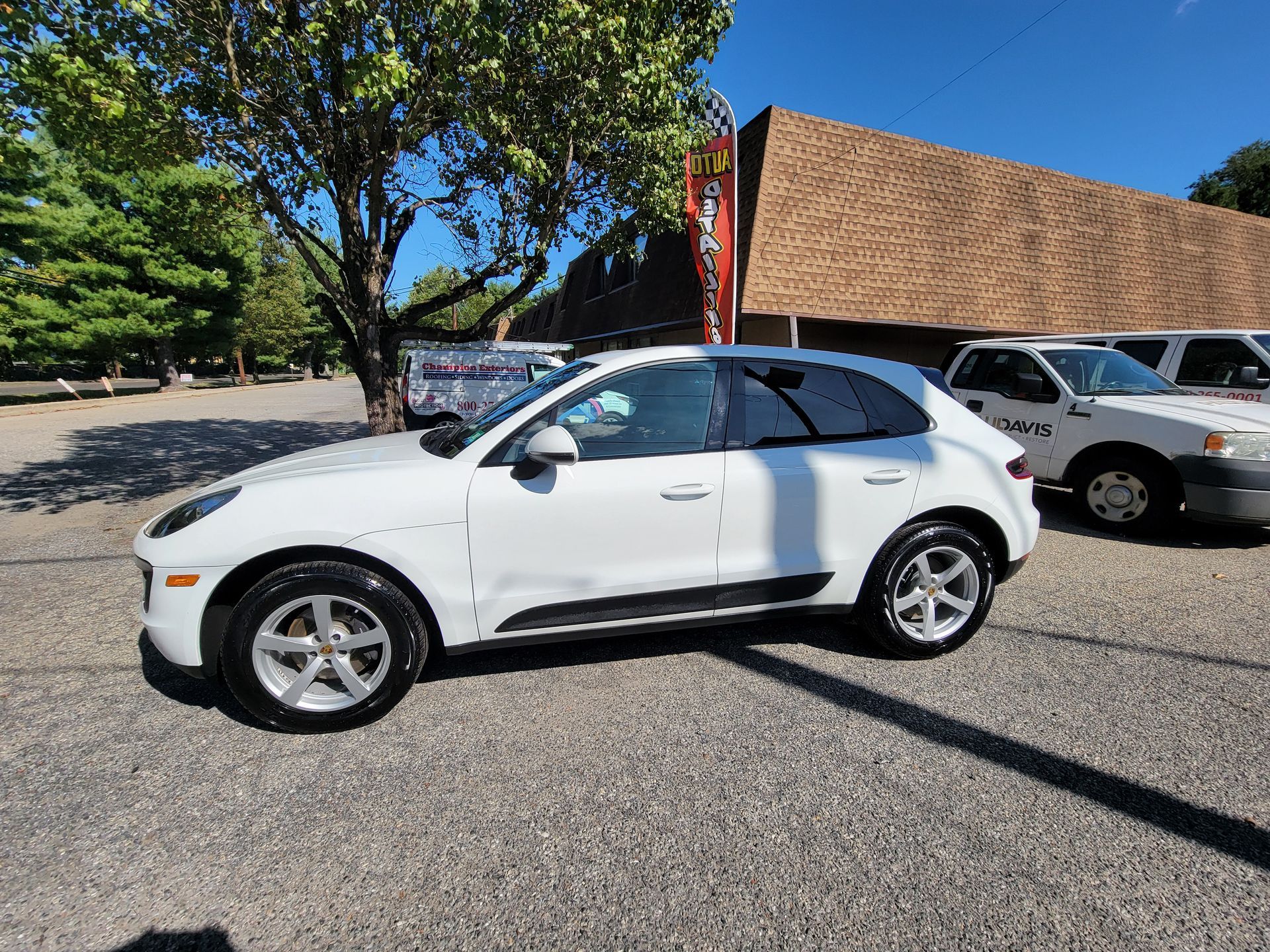 A white porsche macan is parked in a parking lot in front of a building.