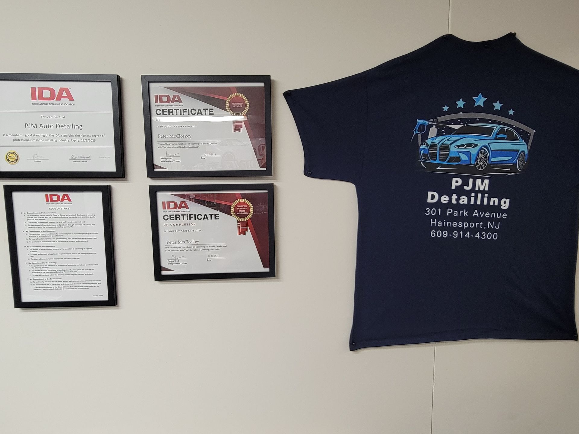 A t-shirt that says pjm detailing is hanging on a wall.