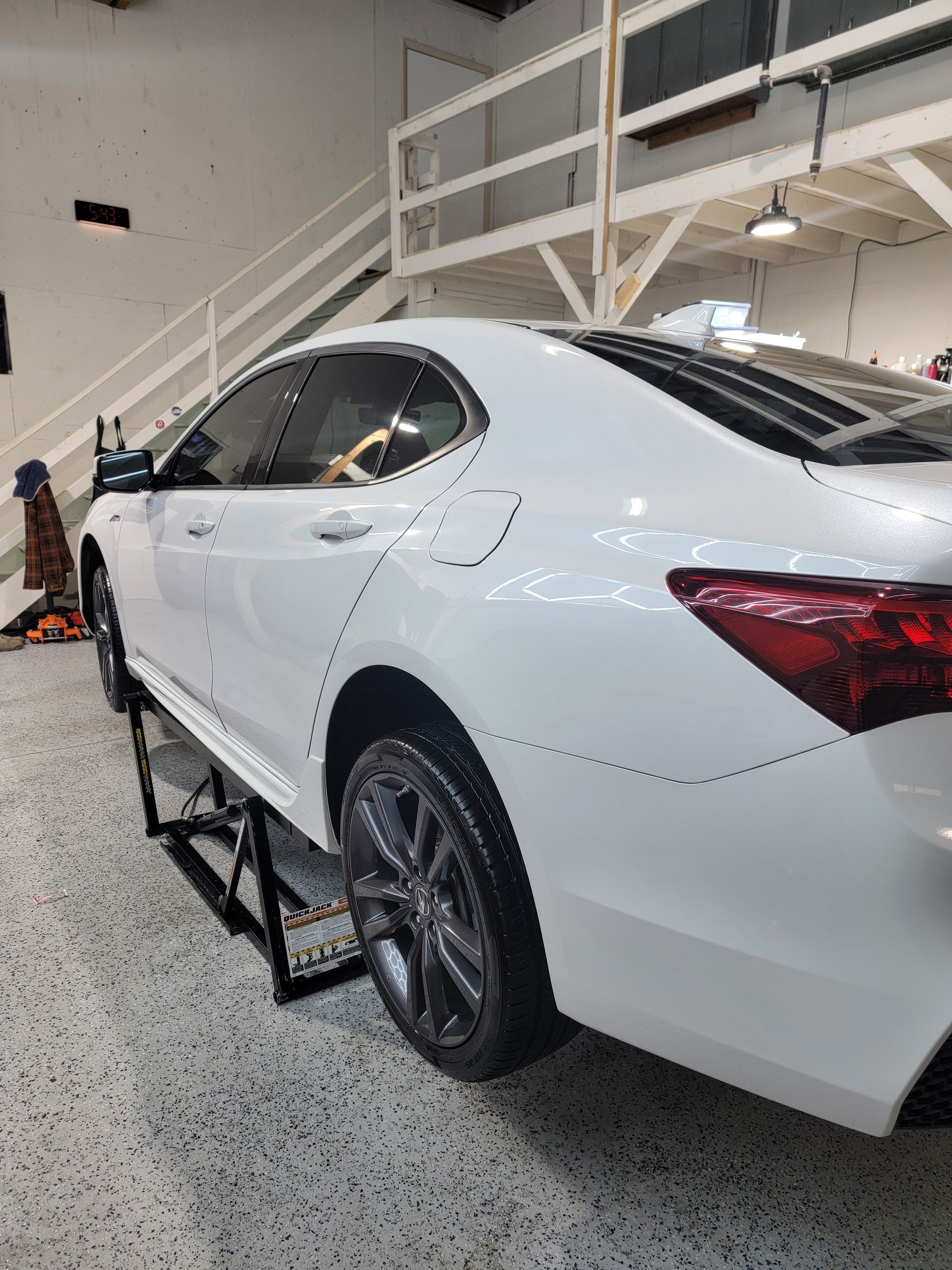 A white car is parked on a ramp in a garage.