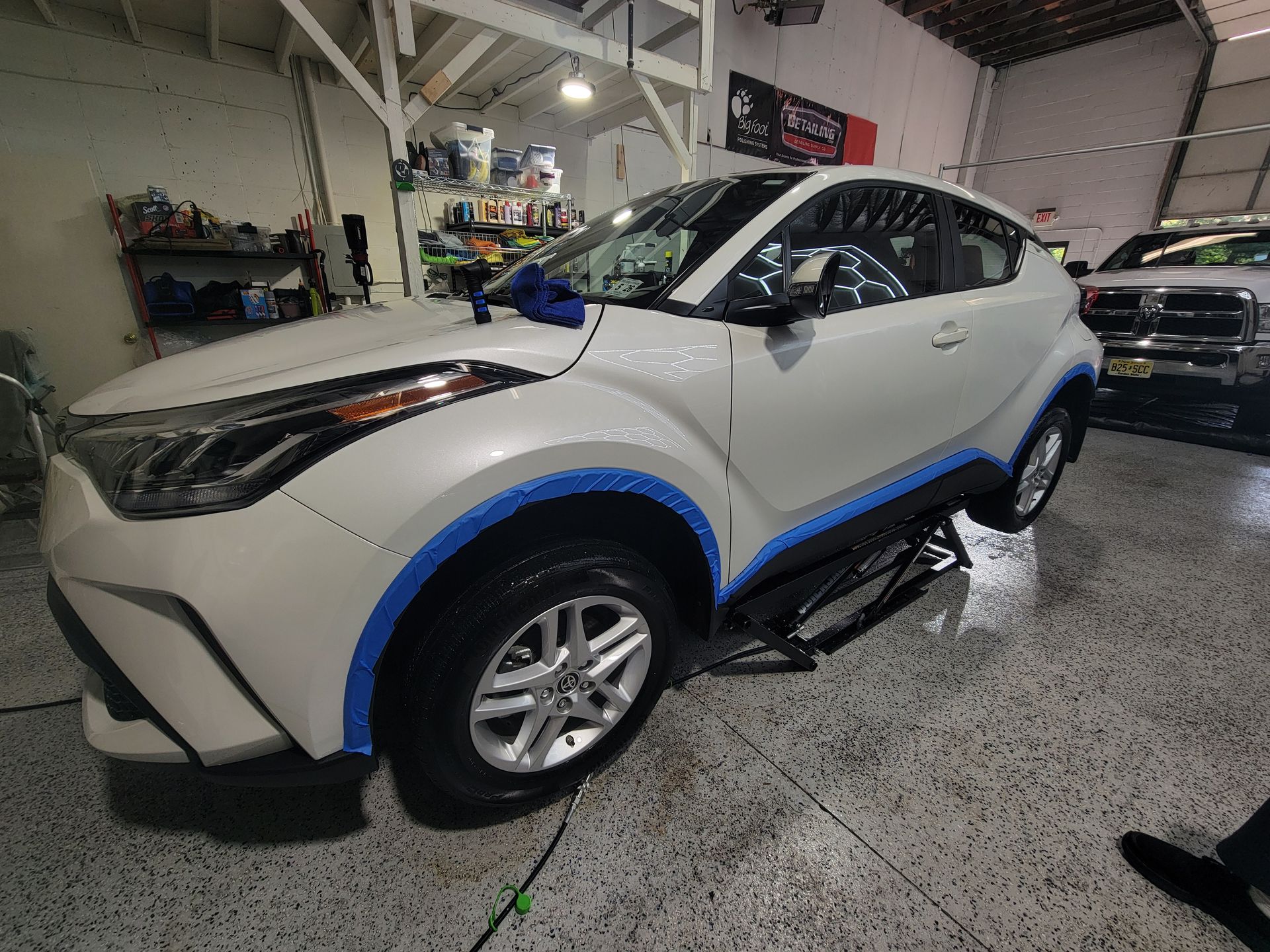 A white car is sitting in a garage with blue tape on the fenders.