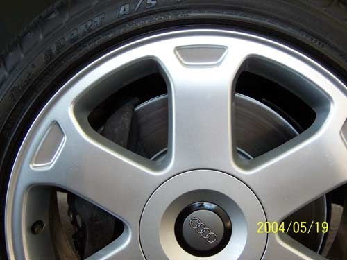 Silver car wheel with the Audi logo, showing the brake disc behind the spokes.