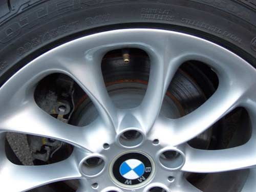 Silver BMW wheel with blue and white logo, tire, and brake rotor visible.