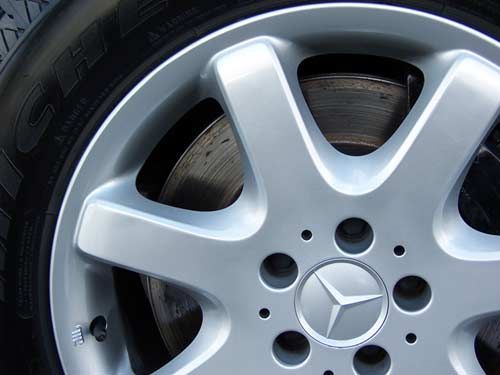 Silver Mercedes-Benz car wheel with a tire and brake disc in focus.