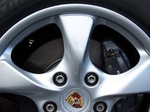 Silver car wheel with Porsche logo, visible brake disc and caliper.