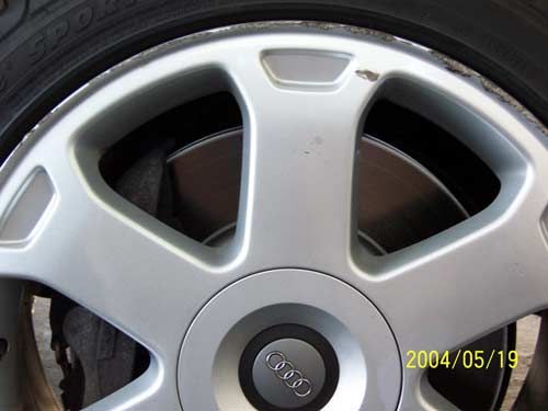 Close-up of a silver Audi car wheel with the brand logo at its center and a visible brake disc.