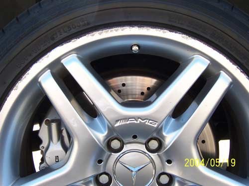 Silver AMG rim and tire with drilled brake rotor and Mercedes-Benz logo.
