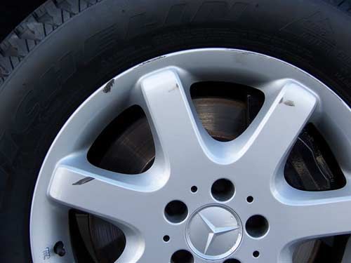 Silver Mercedes-Benz wheel with tire; showing scratches.