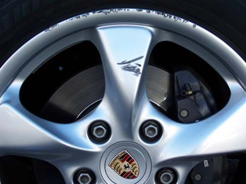 Close-up of a shiny silver Porsche wheel with visible brake components and the Porsche logo in the center.