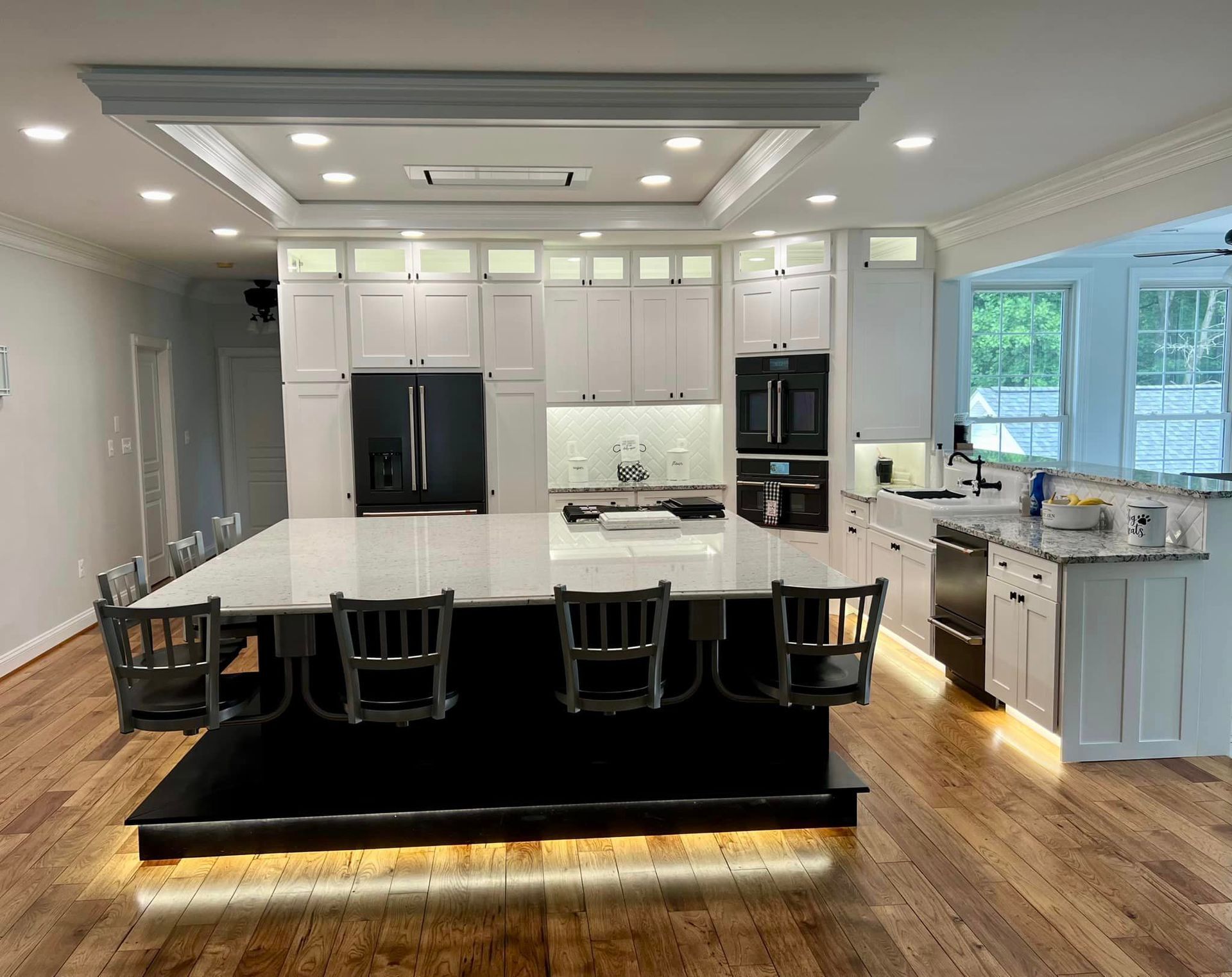 Bright modern kitchen with white cabinets, black island, hardwood floors, and large windows