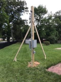 Wooden utility pole with guy wires and electrical boxes in a grassy yard