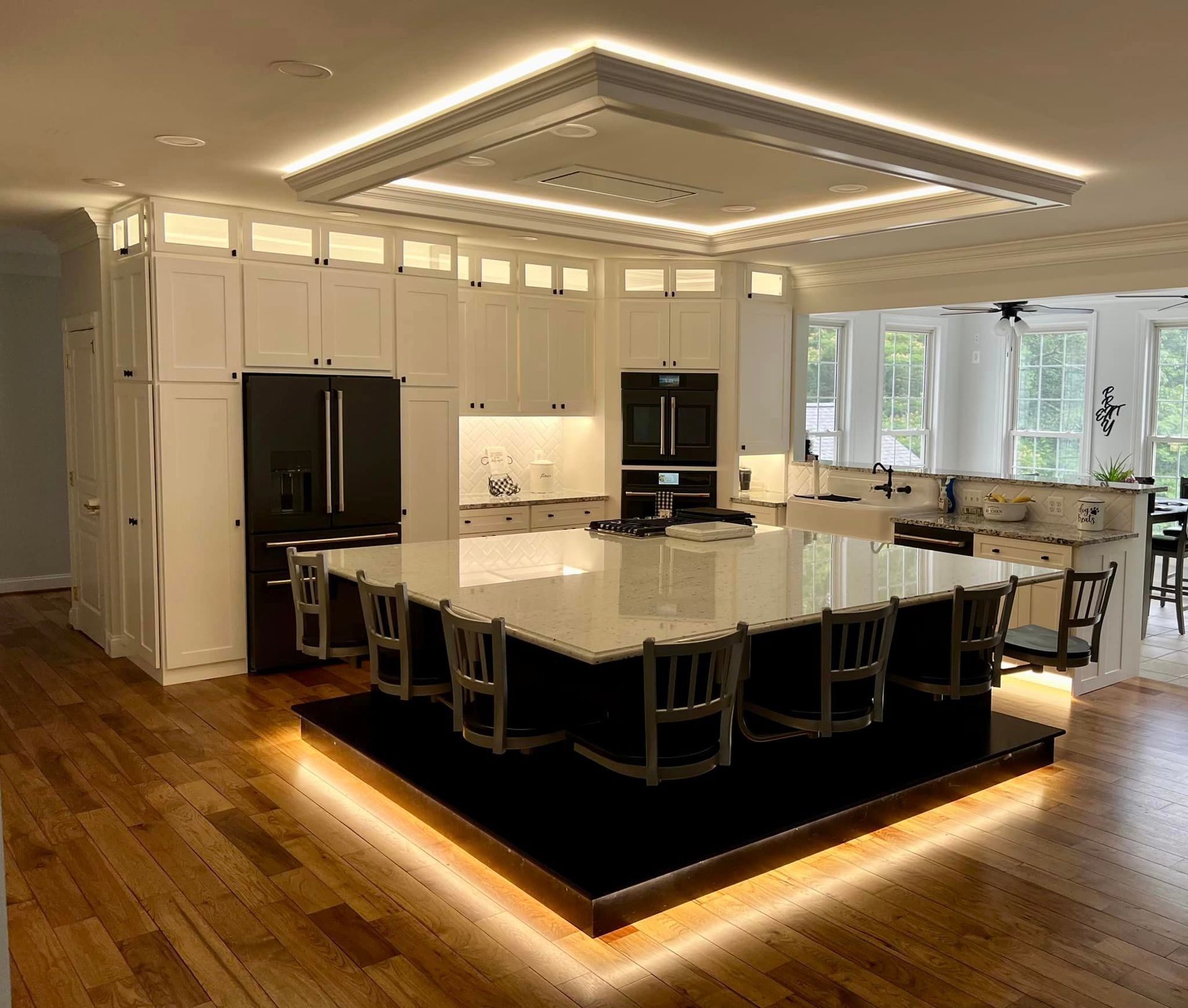 Modern kitchen with a large island, black chairs, white cabinets, and warm under-cabinet lighting