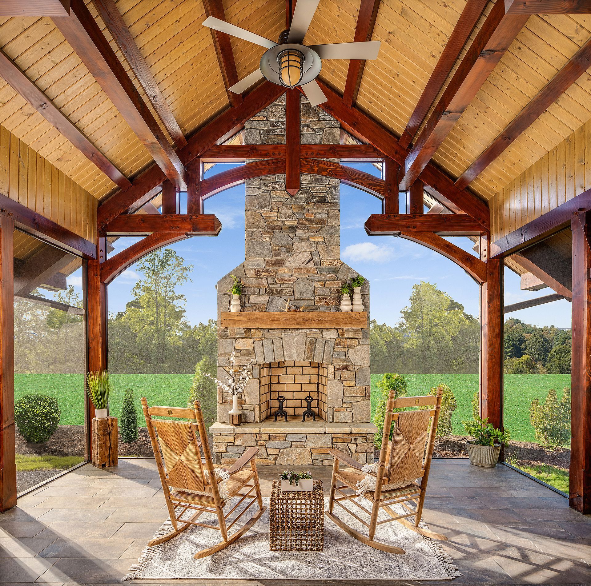 A covered patio with a stone fireplace and rocking chairs.