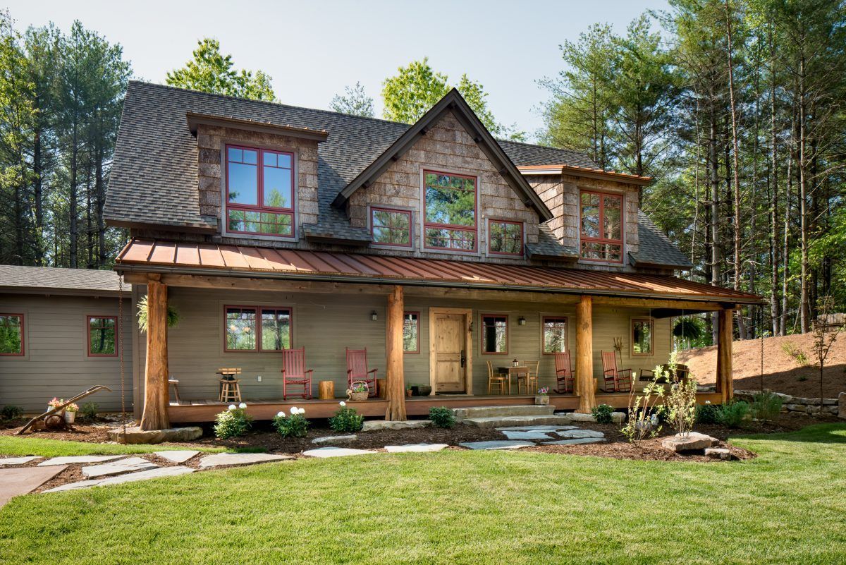 A large house with a large porch in the middle of the woods.