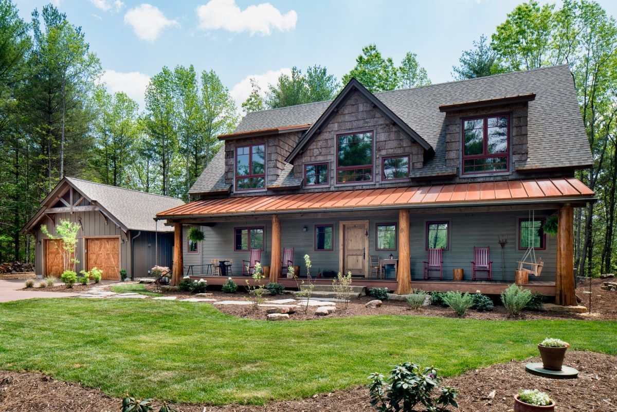 A large house with a large porch in the middle of a lush green field.