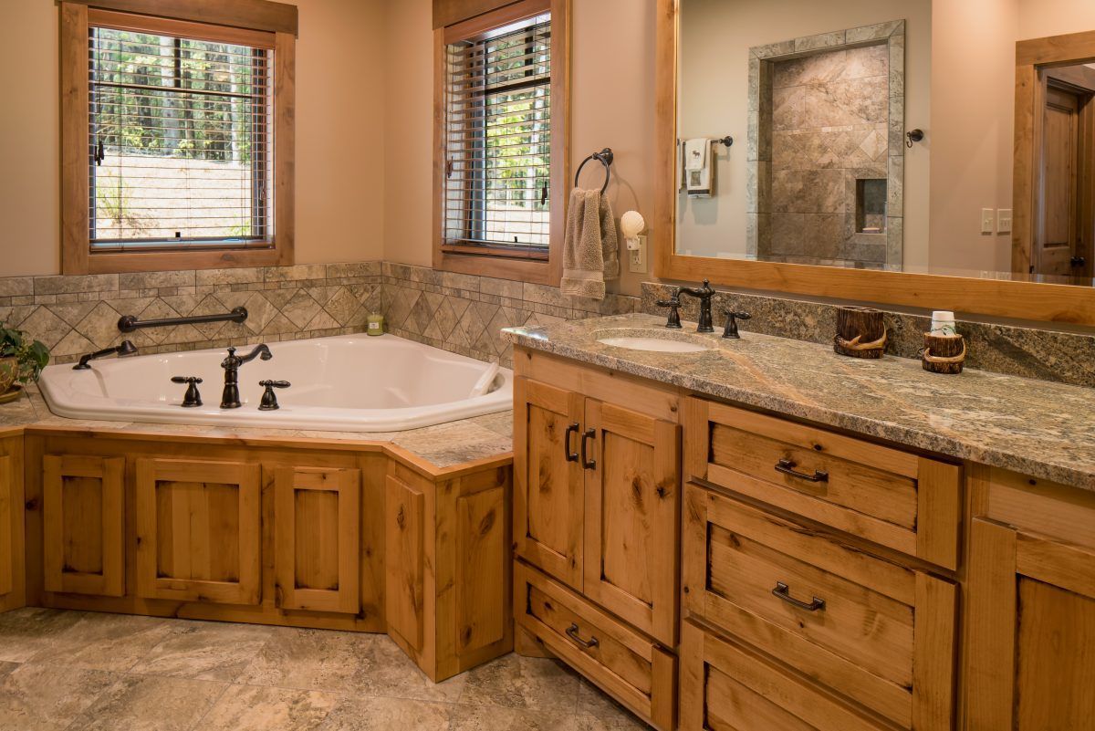A bathroom with a tub, sink, mirror, and wooden cabinets.