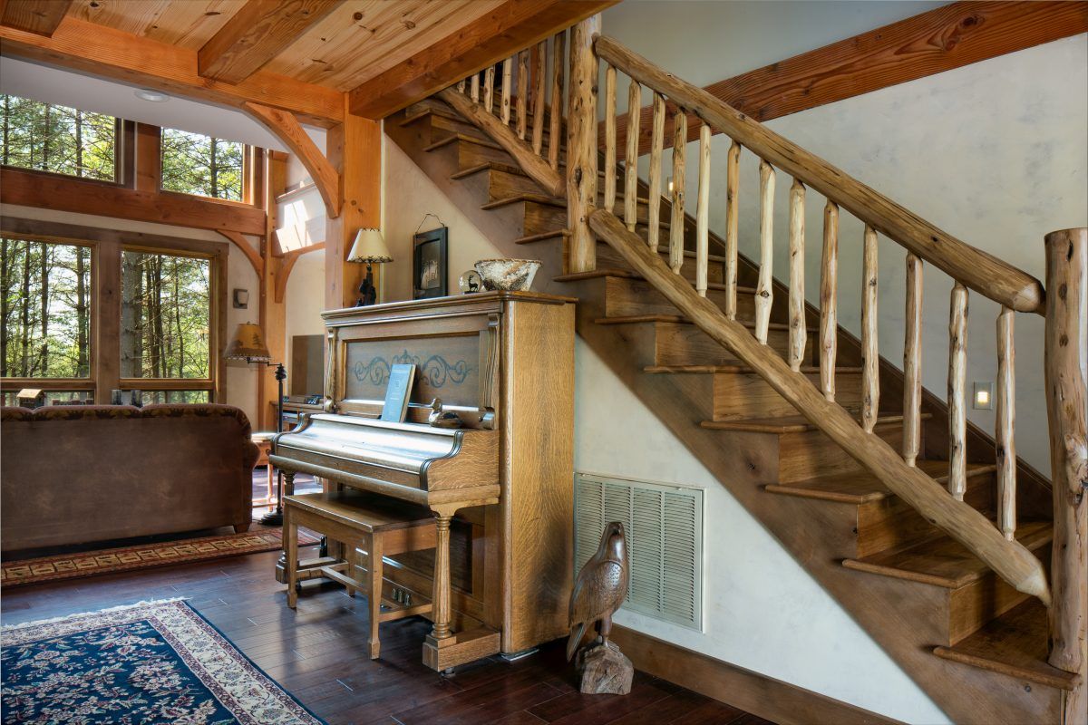 A piano is sitting under a wooden staircase in a living room.