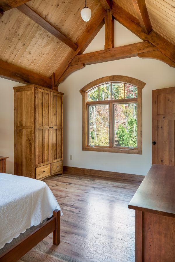 A bedroom with a vaulted ceiling and a large window.