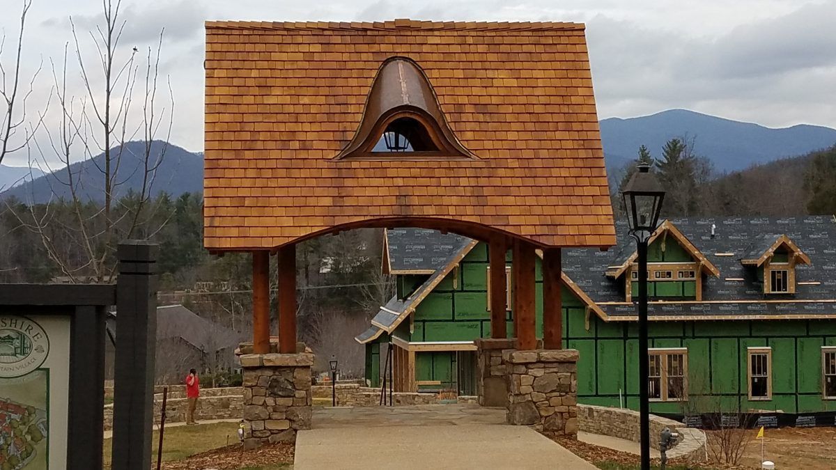 A wooden archway leading to a house under construction with mountains in the background.